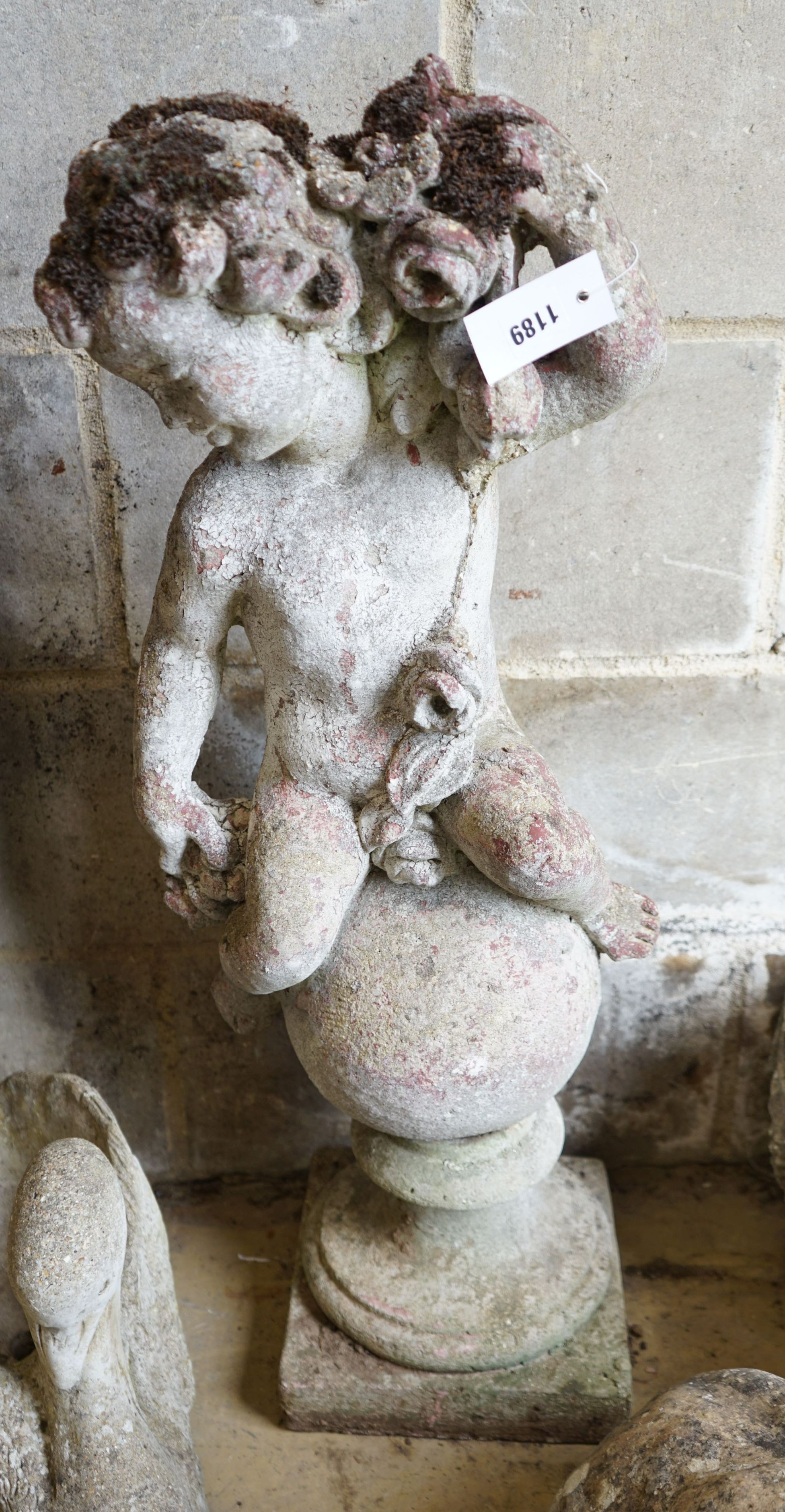 A reconstituted stone seated cherub and orb garden ornament, height 84cm